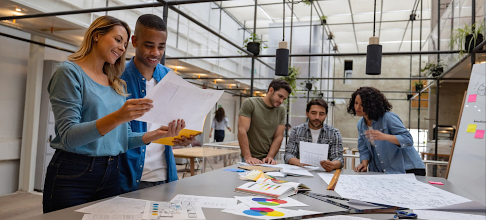 [Featured image] A team of UX designers works on app wireframes at a table in a brightly lit office.