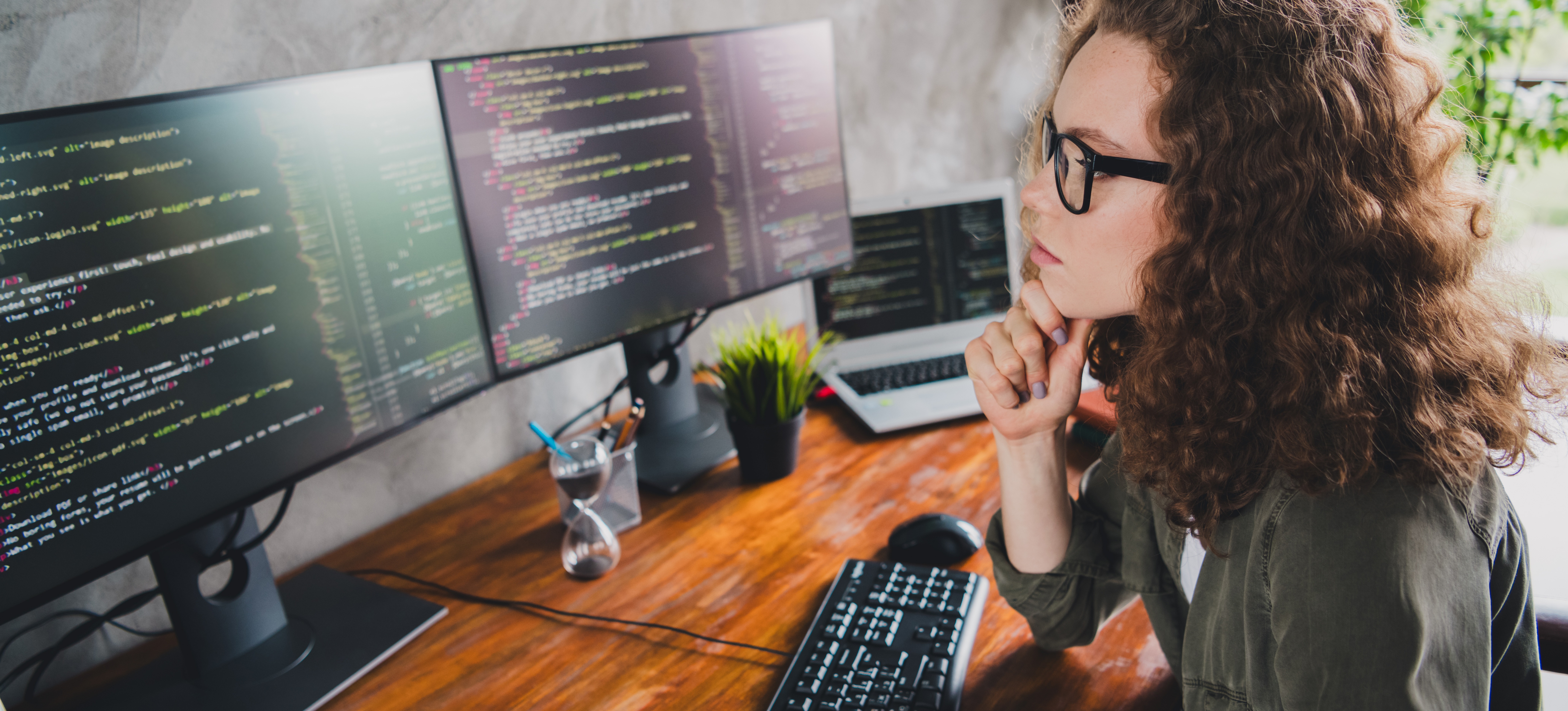 [Featured Image] A data analyst wearing glasses ponders as she looks at her two computer screens and works with A/B testing tools.