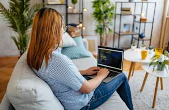 [Featured image] A woman sits on a sofa with a laptop working as a cybersecurity analyst.