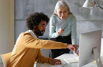 [Featured Image] Two coworkers look at a desktop computer display.