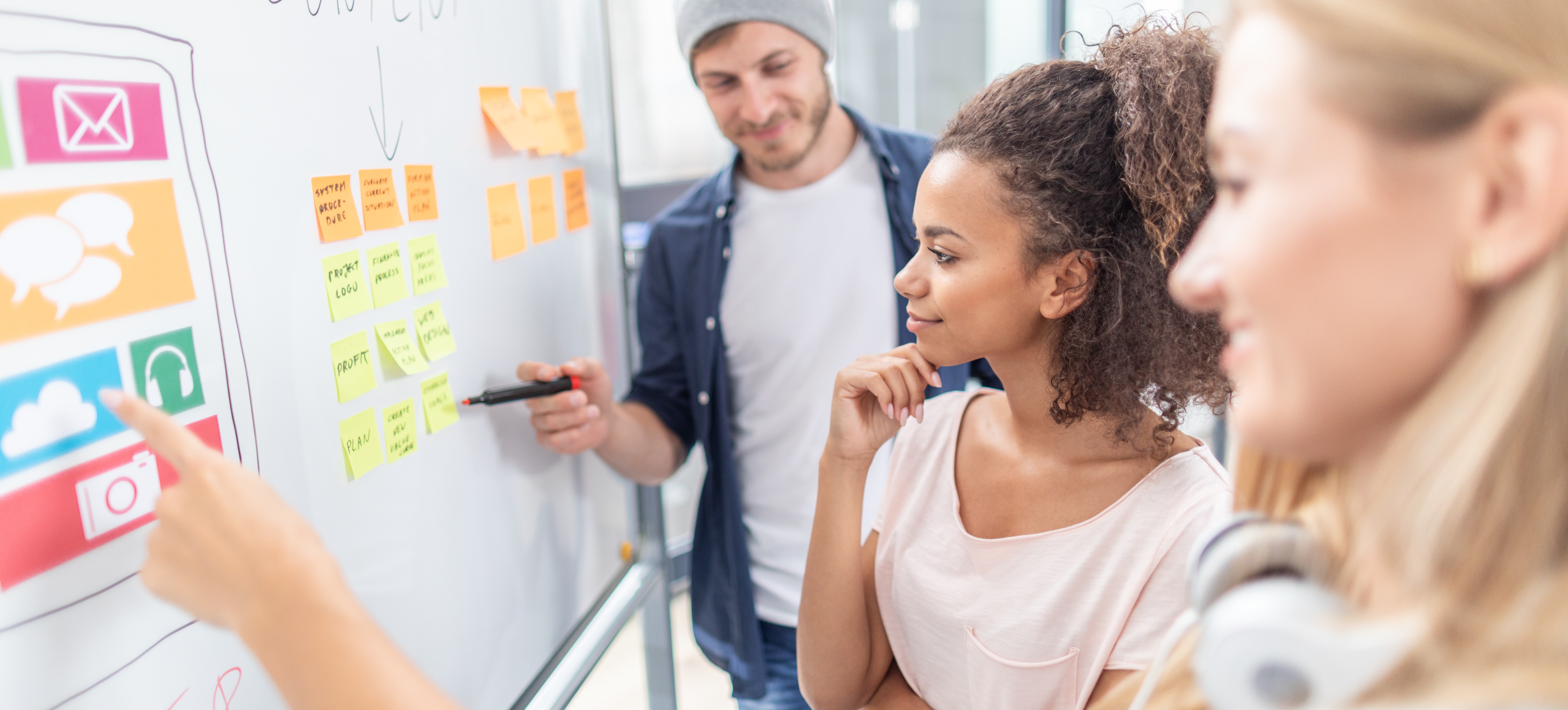 [Featured Image] A content marketing specialist and two colleagues stand in front of a whiteboard discussing content strategy for a website.