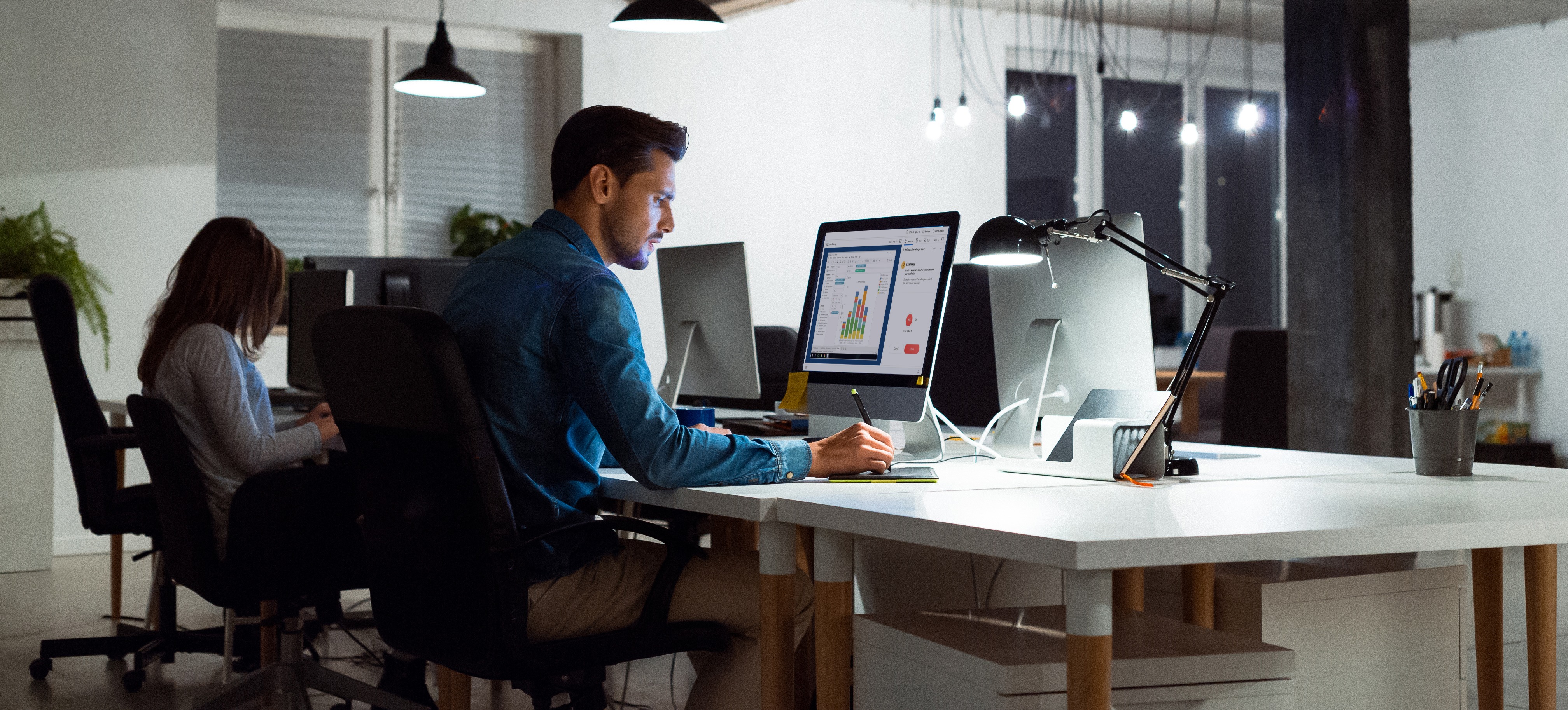 [Featured Image]:  A worker wearing a blue shirt is sitting in front of their desktop, performing their duties as a data analyst. 