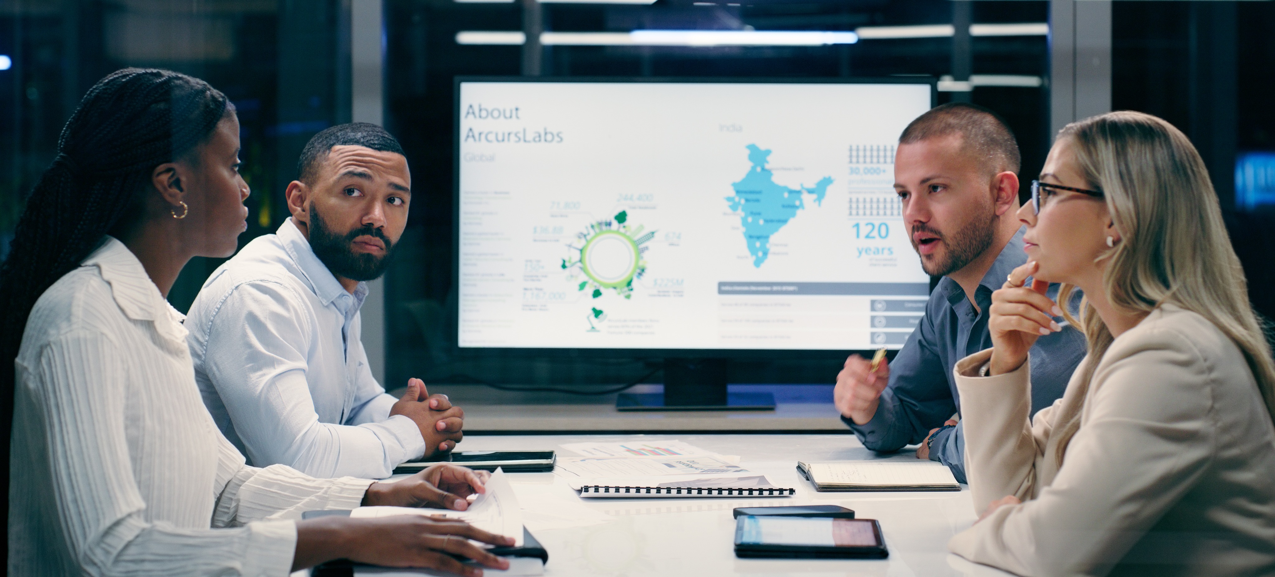 [Featured Image] Professionals in a work environment having a meeting discussing database management tools while a screen in the background displays relevant data.
