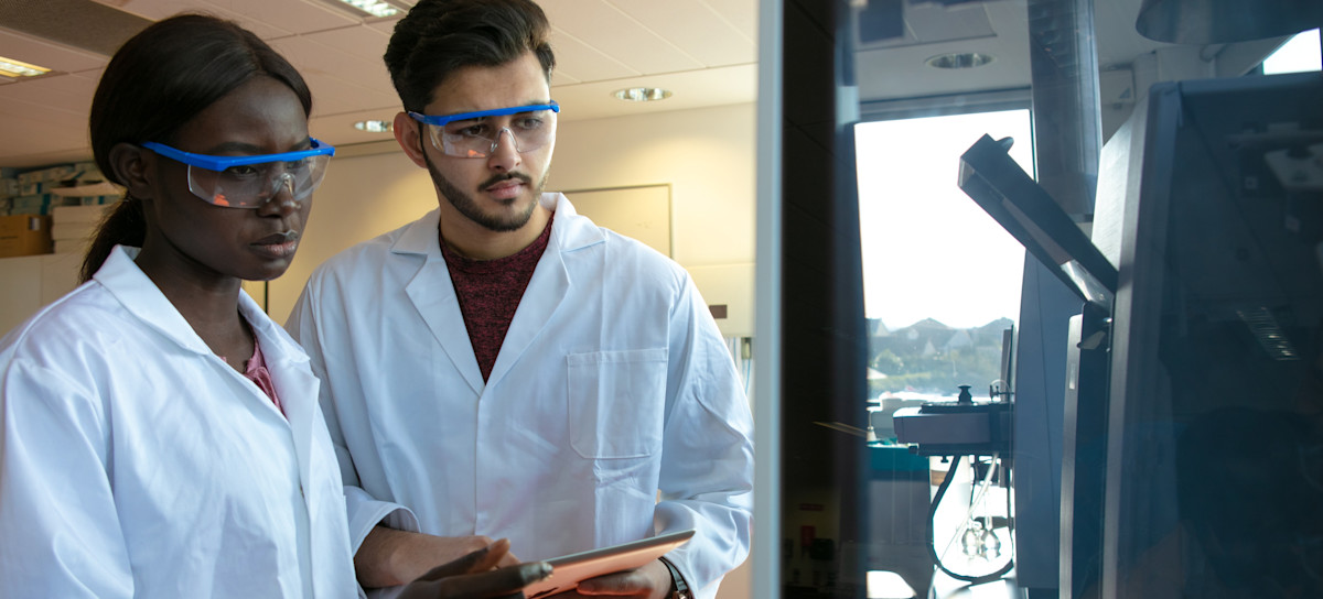 [Featured image] Two public health bachelor's degree holders in protective goggles work in a scientific lab.