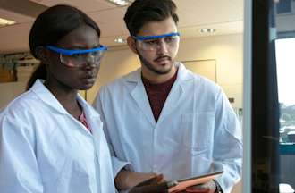 [Featured image] Two public health workers in protective goggles work in a scientific lab.