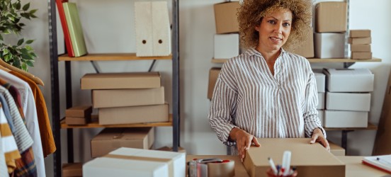 [Featured image] A woman in a striped shirt selling clothes as a side hustle prepares a shipment for a customer.