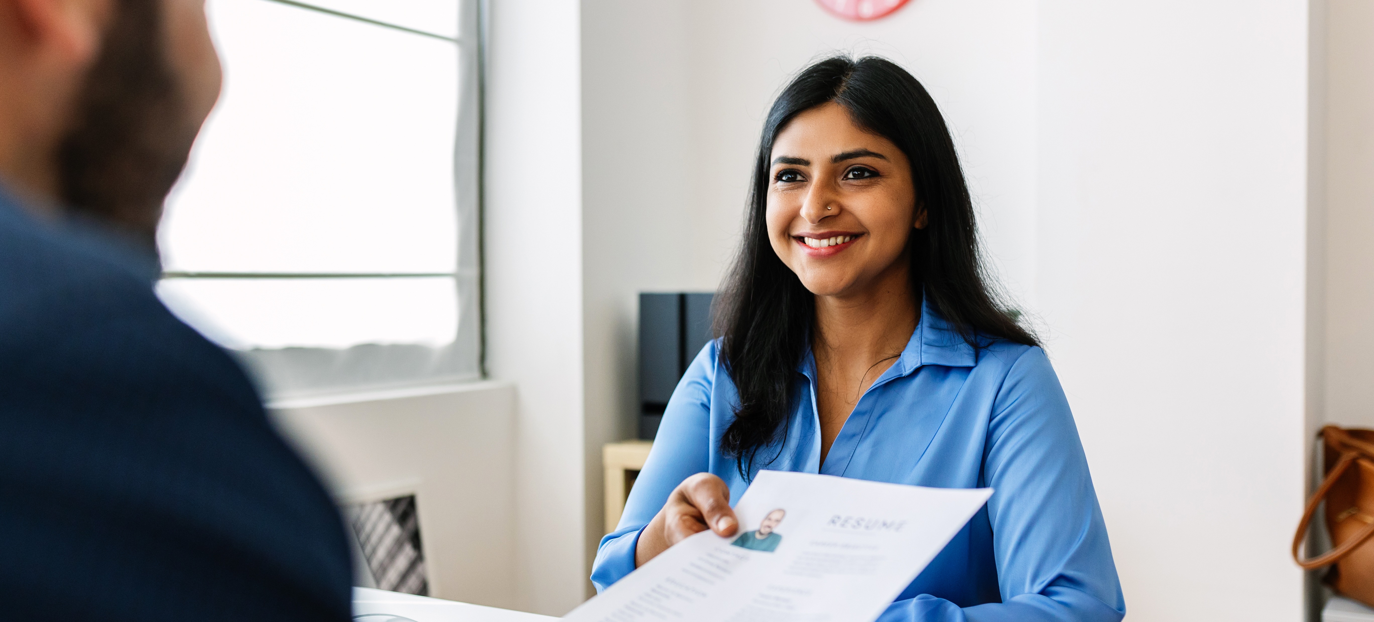 [Featured image] A job candidate is seen giving a resume to the HR manager. 
