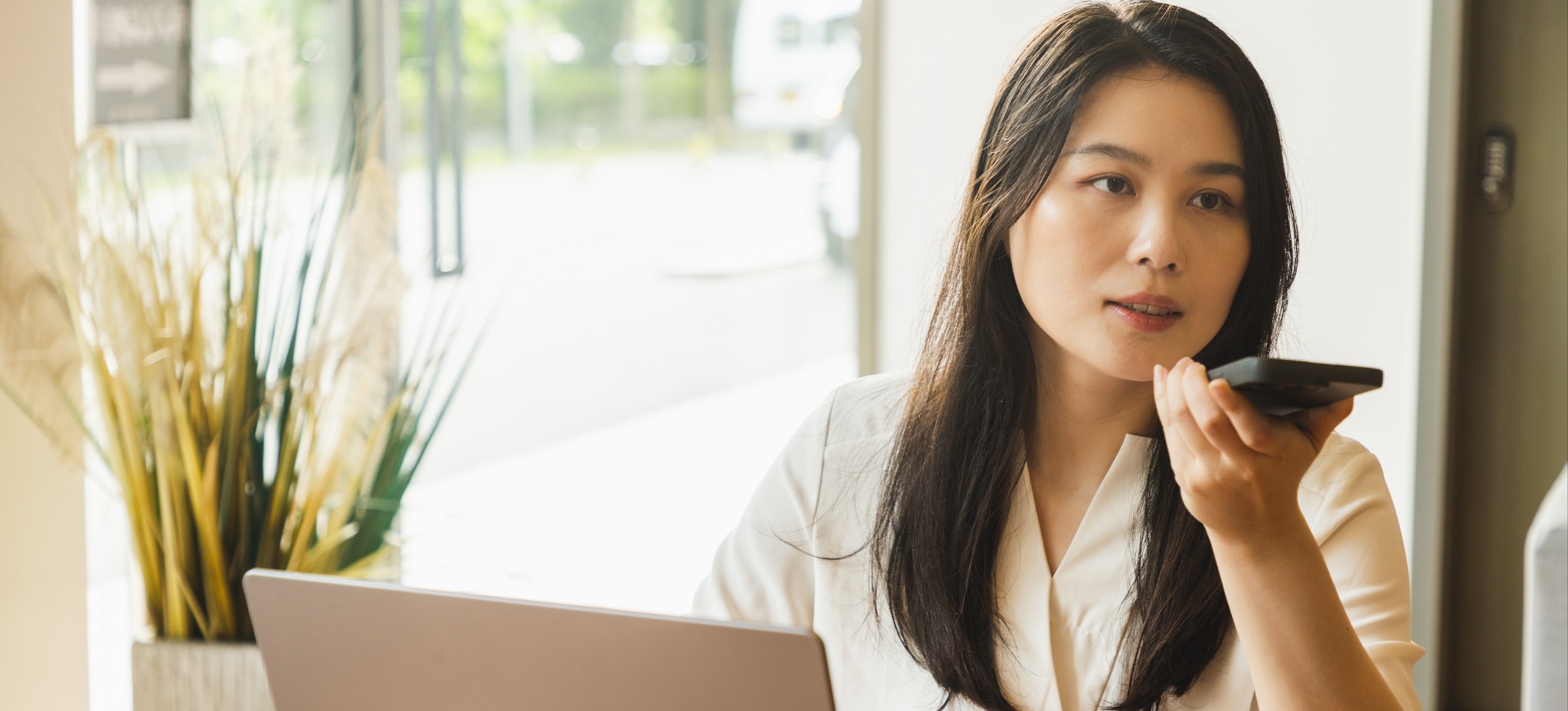 [Feature Image: woman using an AI assistant on her smartphone while working]
