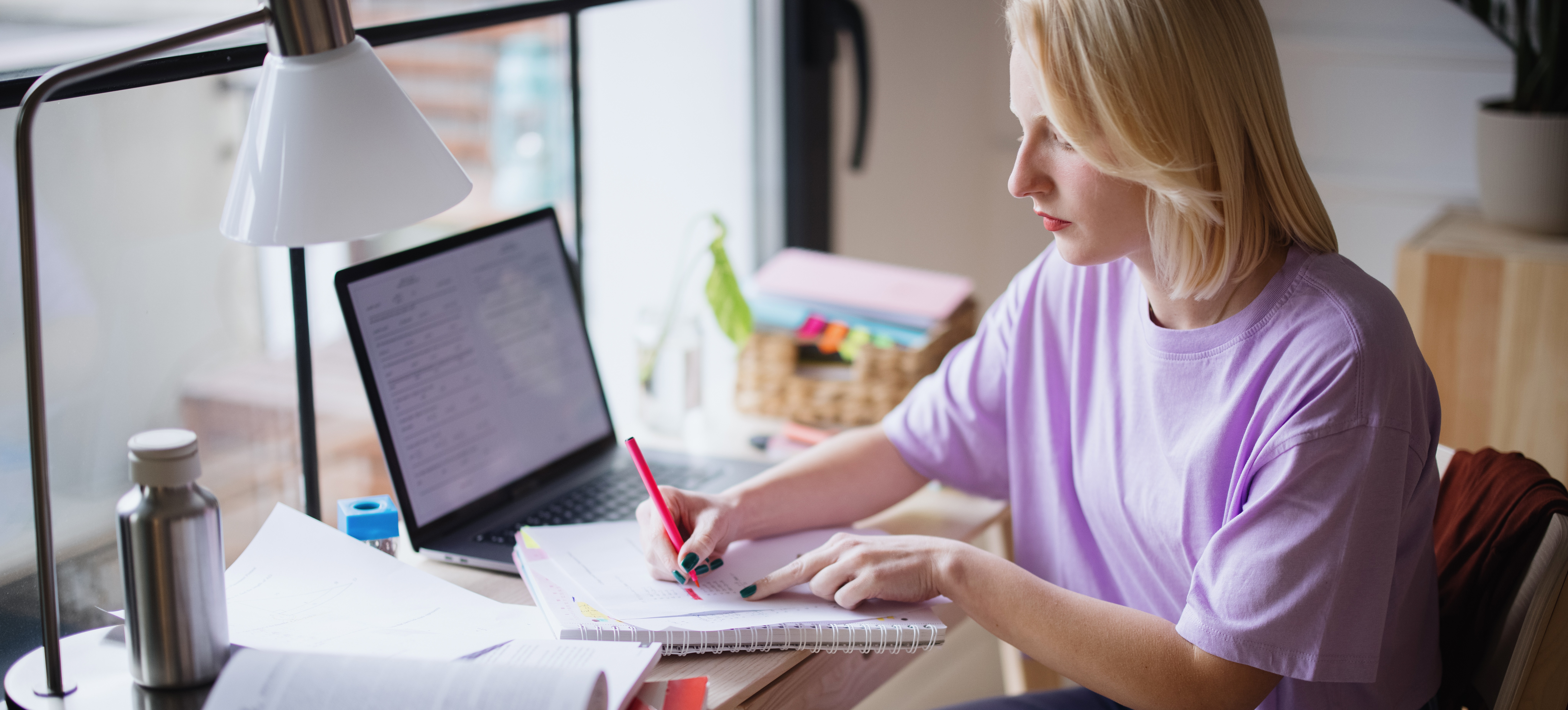 [Featured image] A student working on their entrepreneurship degree studies at a desk with a notebook, textbook, and laptop.