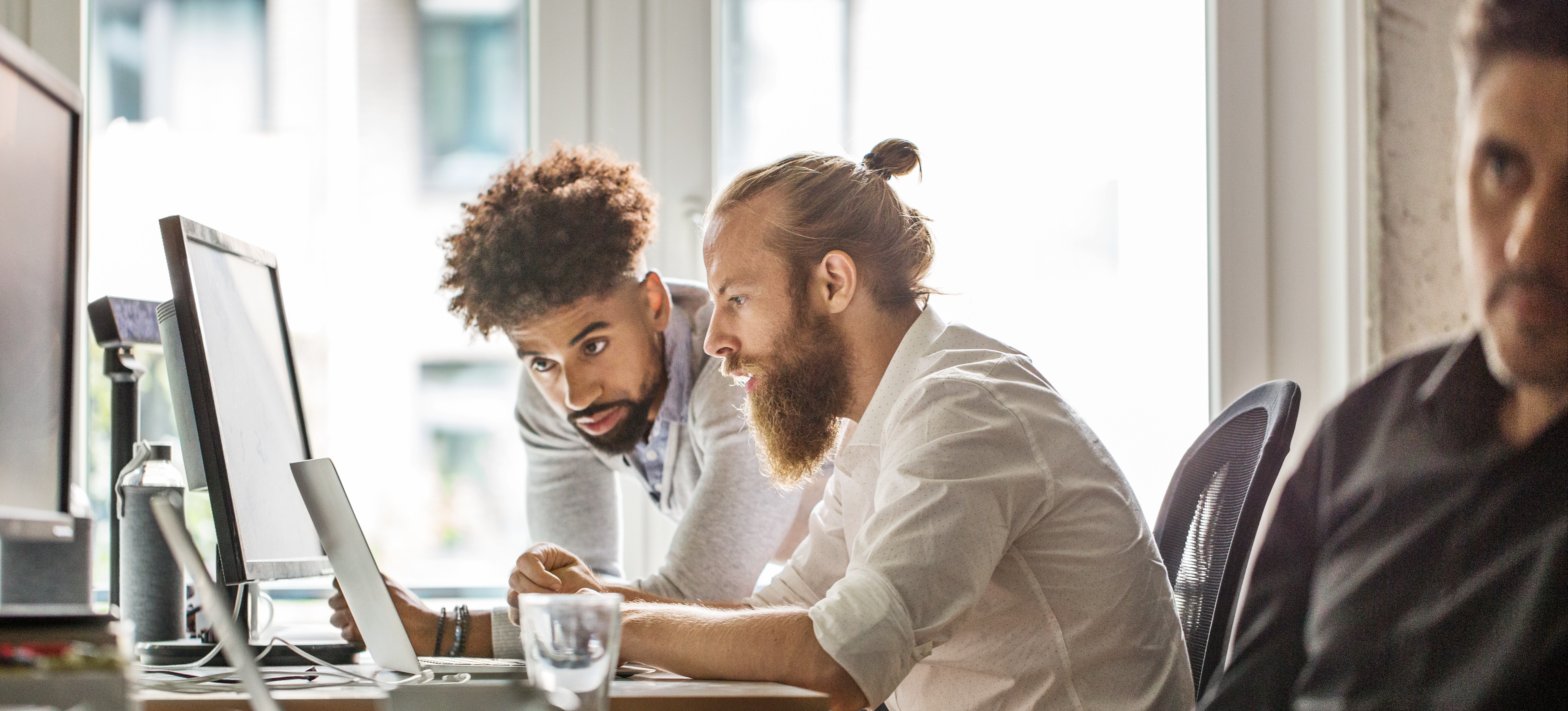 [Featured image] Two coworkers looking at a laptop while discussing NLU vs NLP and how the technologies differ. 
