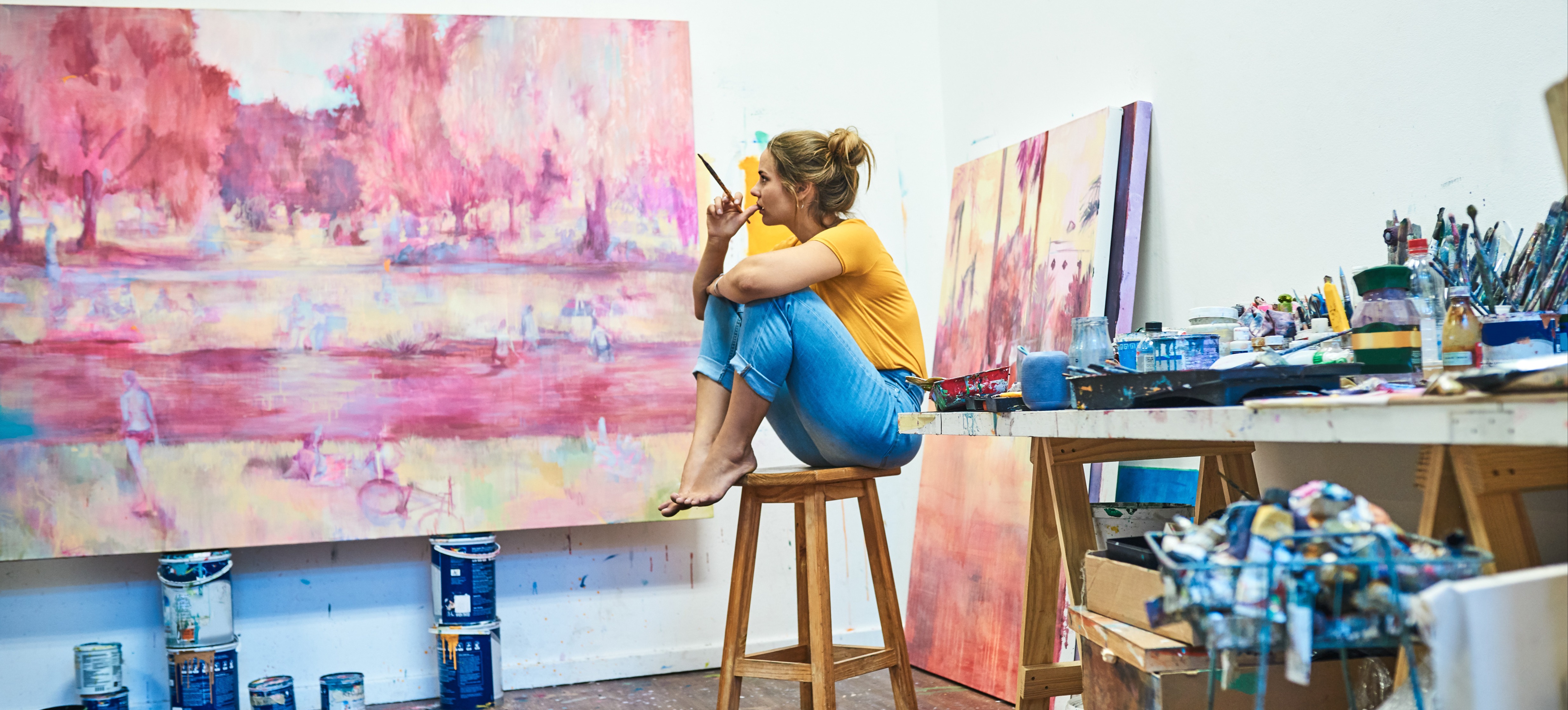 [Feature Image] An aspiring artist in an MFA degree program works on a project that’s part of their studies in a painting studio.

