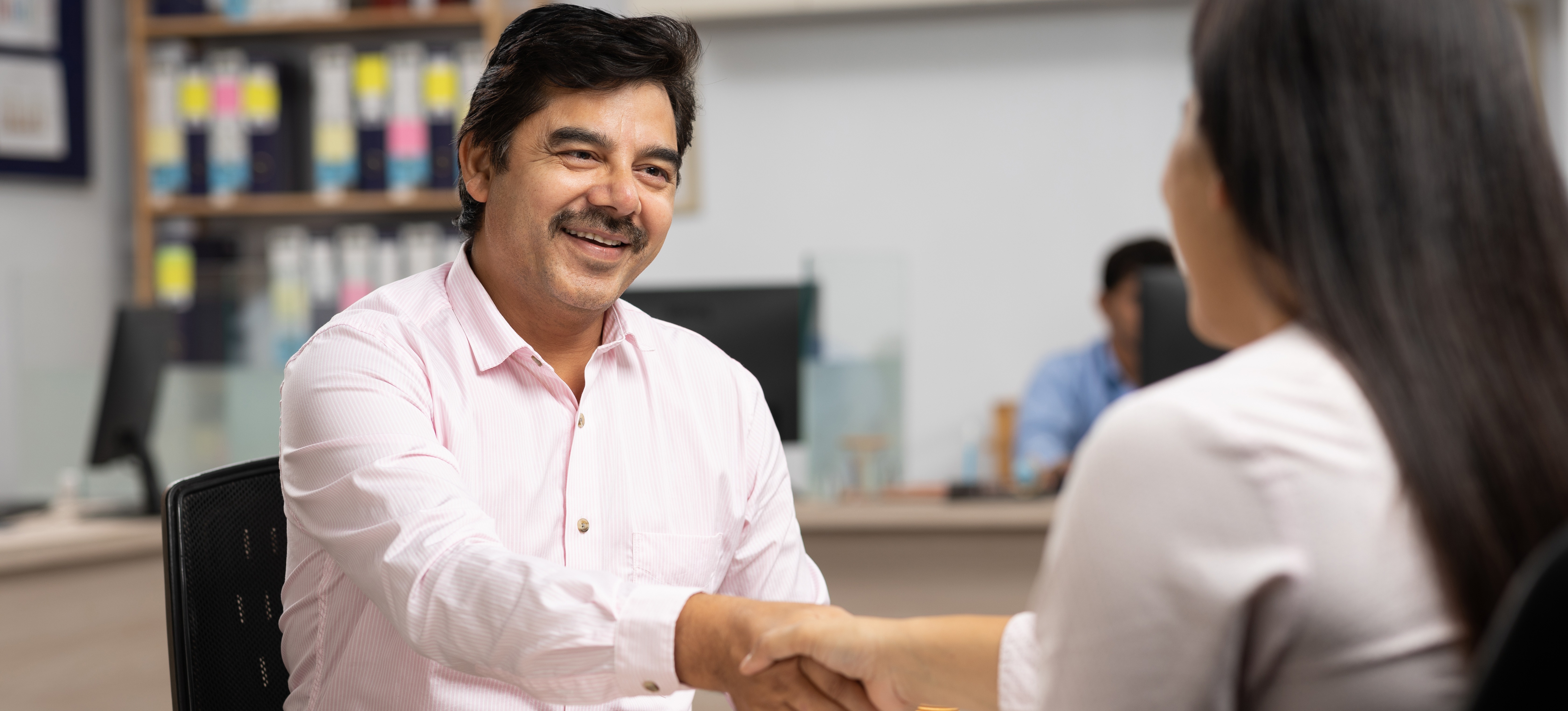[Featured Image] A smiling job candidate shakes an interviewer's hand after using the right CV keywords to get past the ATS and land the meeting. 
