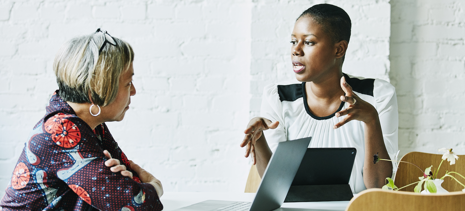 [Featured image] A business analyst interviews an employee. Both have their laptops in front of them.