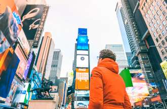 [Featured image] A man in an orange parka stands in Times Square looking up at the advertisements.