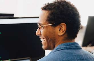 [Featured Image] A software engineer smiles in front of a computer monitor with code on the screen. 