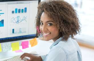 [Featured image] A marketer in a denim shirt reviews marketing analytics from a digital campaign on a desktop computer covered in colored sticky notes.