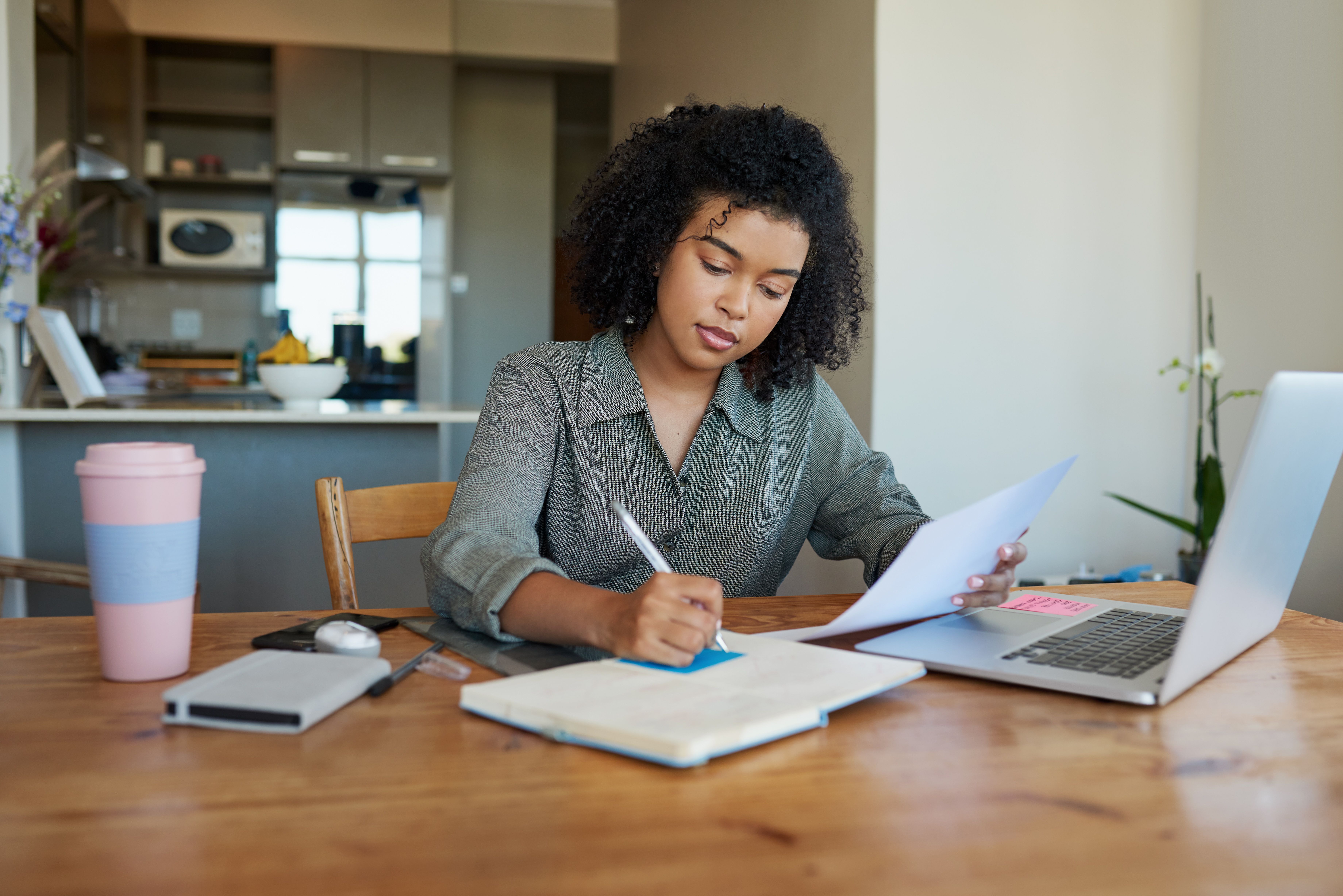 [Featured Image] A woman is writing on a sticky note and using her laptop.