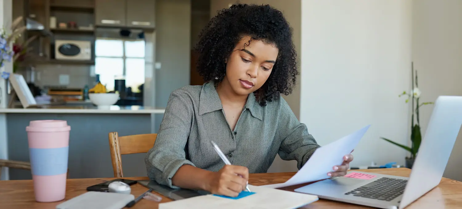 [Featured Image] A person is writing on a sticky note and using their laptop.