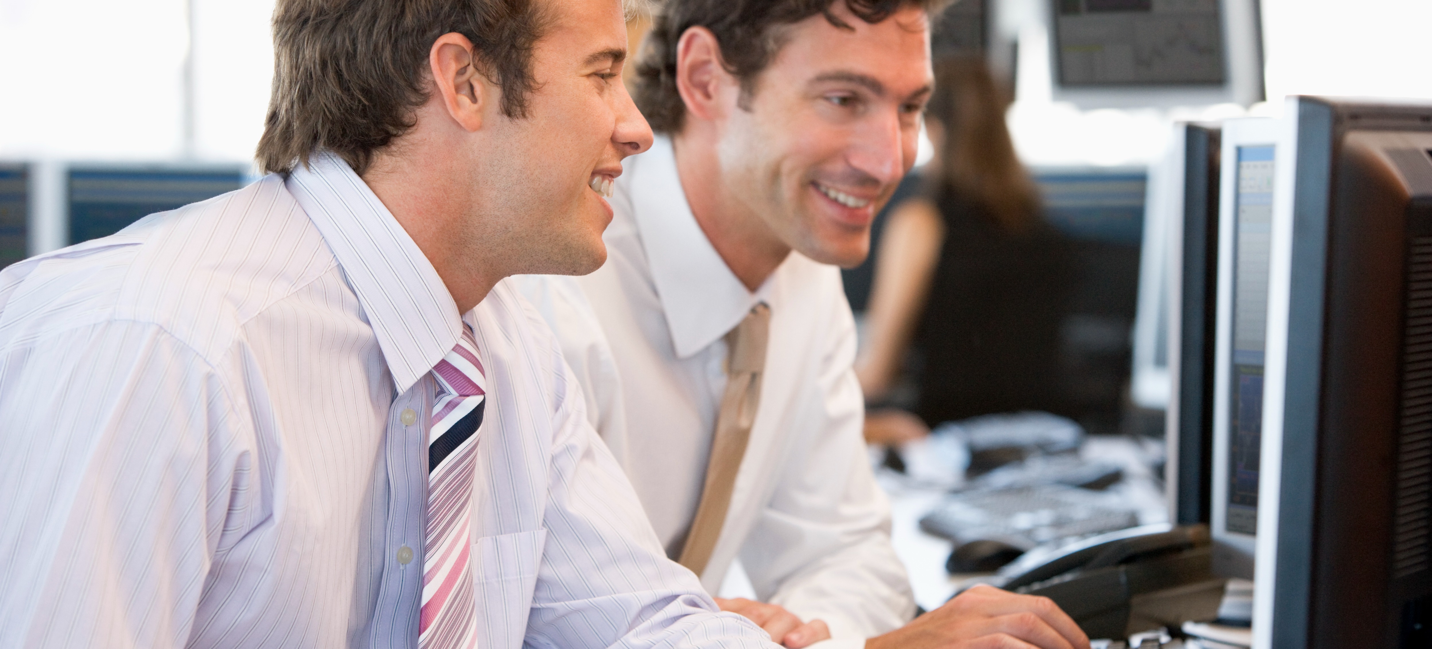 [Featured Image] Two smiling information systems auditors in business attire look at a computer screen in a busy office as they discuss CISA salary figures.
