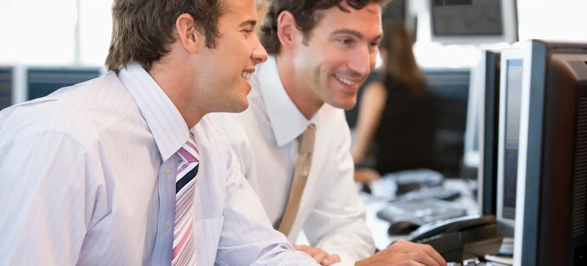 [Featured Image] Two smiling information systems auditors in business attire look at a computer screen in a busy office as they discuss CISA salary figures.
