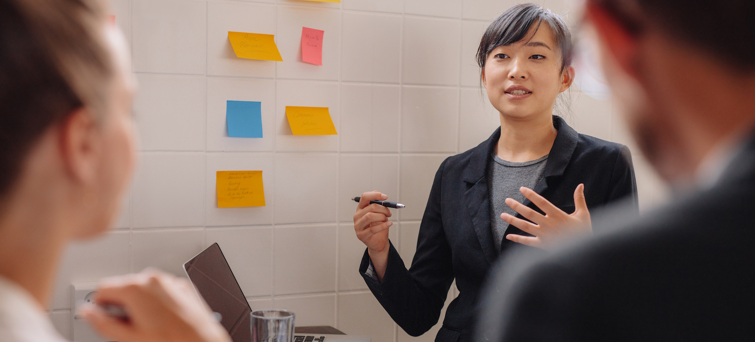 [Featured image] A businessperson dressed professionally stands speaking to two people shown in profile. 