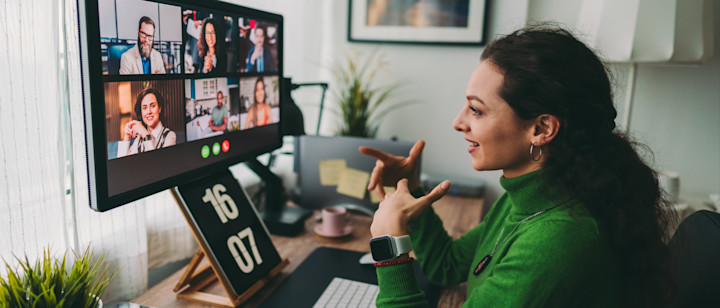 [Featured Image] A woman working remotely at her computer desk attending a virtual meeting. 
