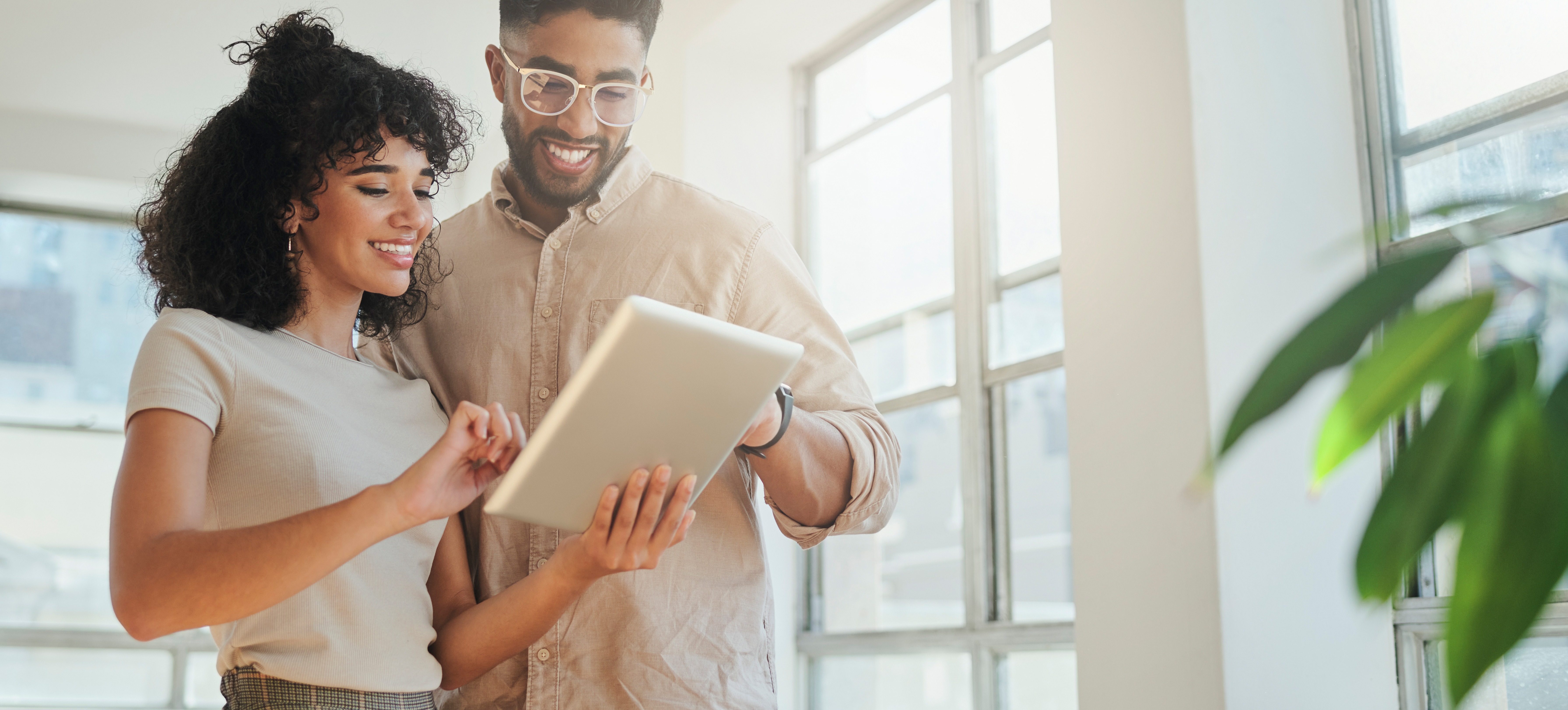 [Featured Image] A smiling HR generalist explains policies to a happy employee while both are looking at a tablet in an office setting.
