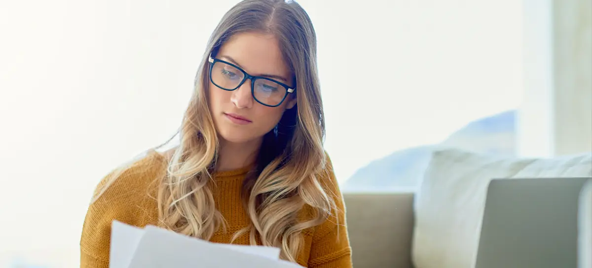 [Featured image] A person in a yellow sweater with glasses, looking at papers, trying to decide how to list references on a resume.