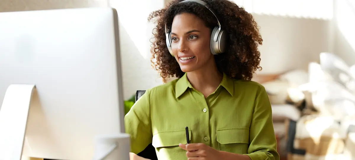 [Featured Image] A professional businesswoman wearing headphones works on her computer on upskilling.
