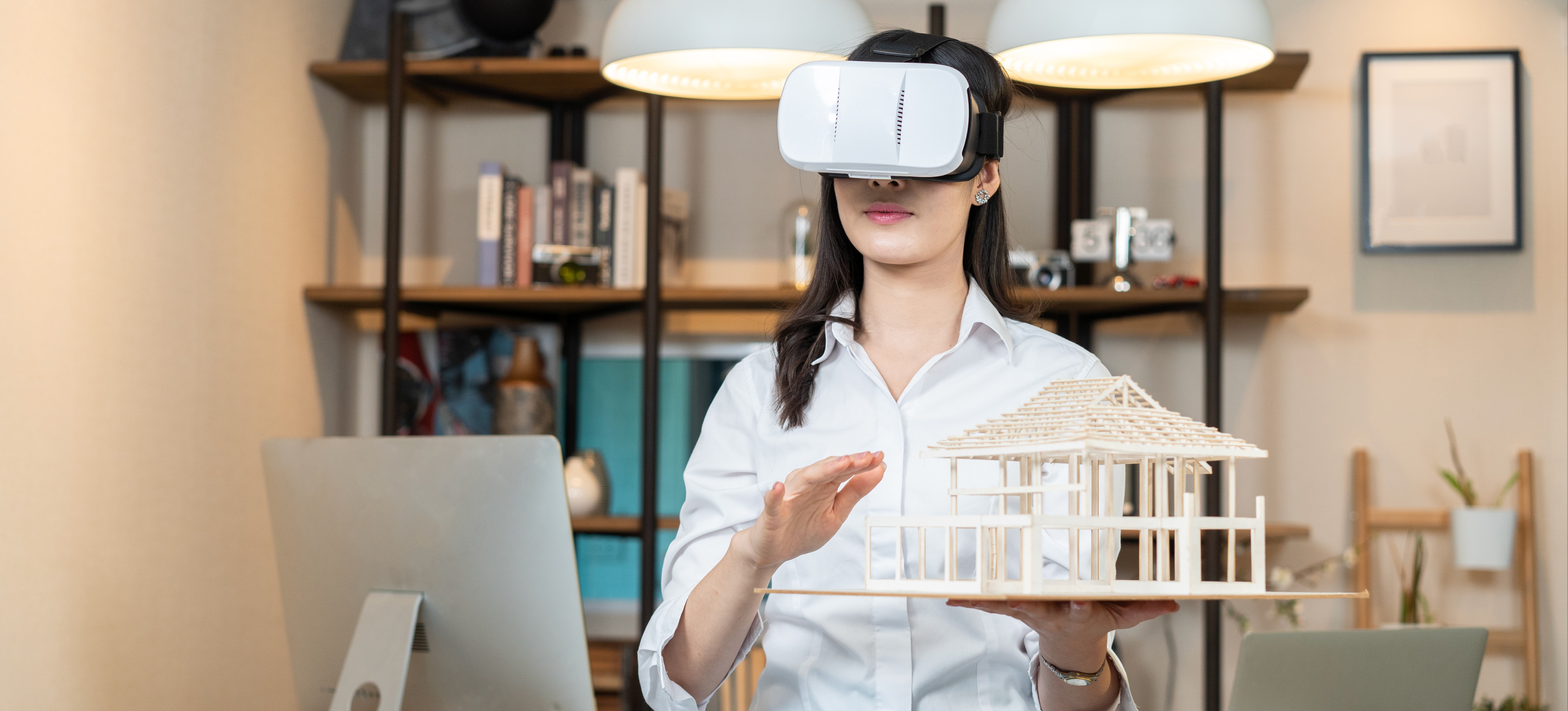 [Featured Image] An architect wearing a VR headset holds a model of a house, demonstrating how virtual reality is used in architectural design and underscoring the impact jobs in virtual reality can have across various industries.