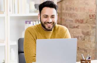 [Featured Image] A man contemplating a job change uses his laptop at home to read a DevOps job description. 
