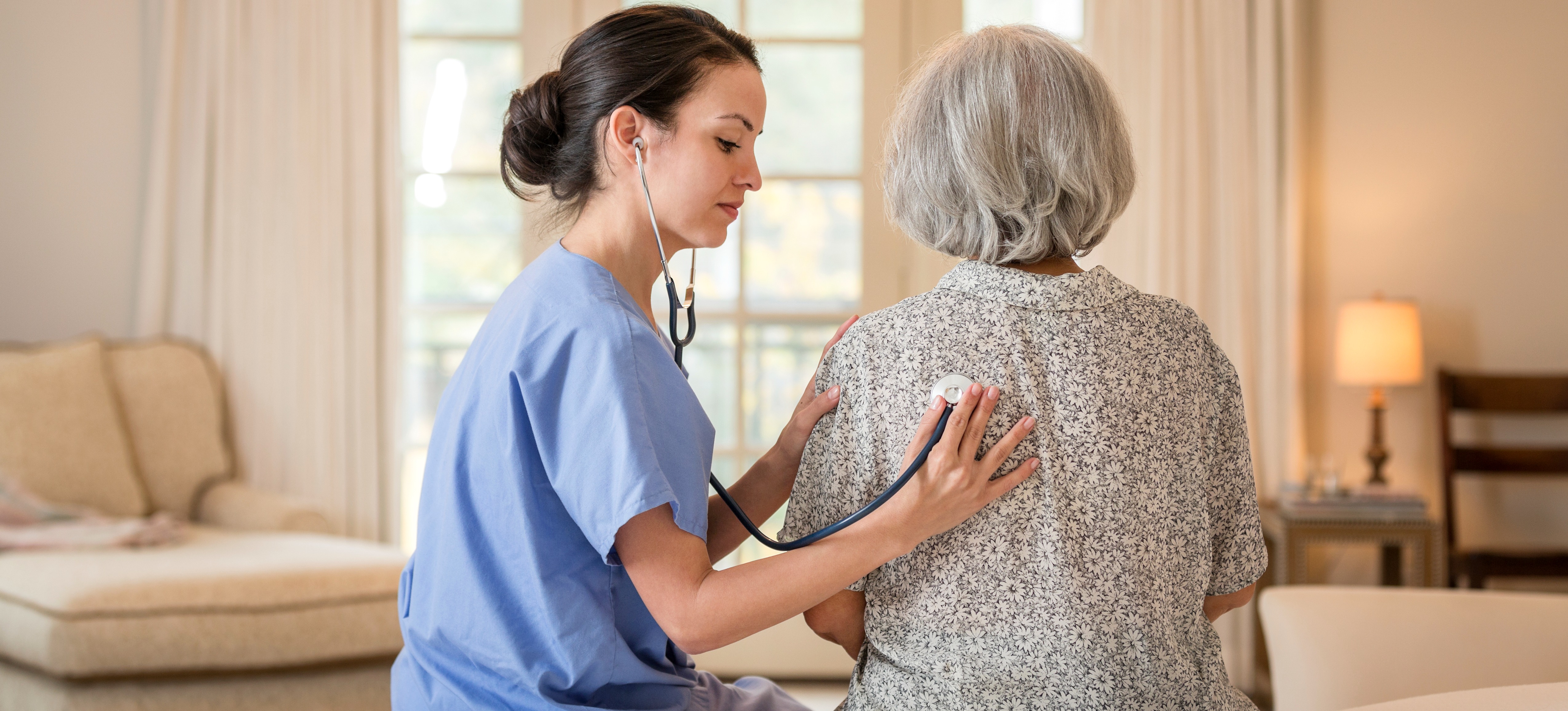 [Featured Image] A physician assistant, one of the biggest jobs in demand in Texas, sits on a bed with a patient and listens to her chest with a stethoscope.
