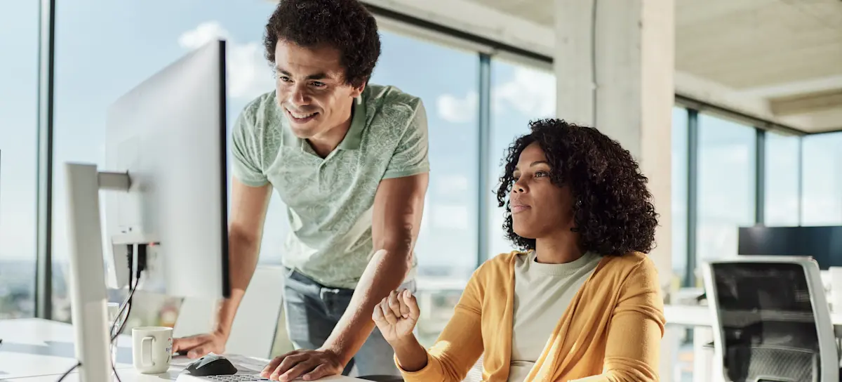 [Featured Image] Two software programmers are discussing the merits of GitLab and GitHub while looking at a computer screen in a workspace with many windows. 
