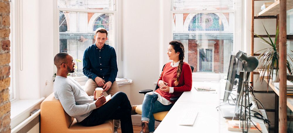 [Featured Image] A group of coworkers in an office discuss the concept of growth mindset and how it contributes to their work everyday. 