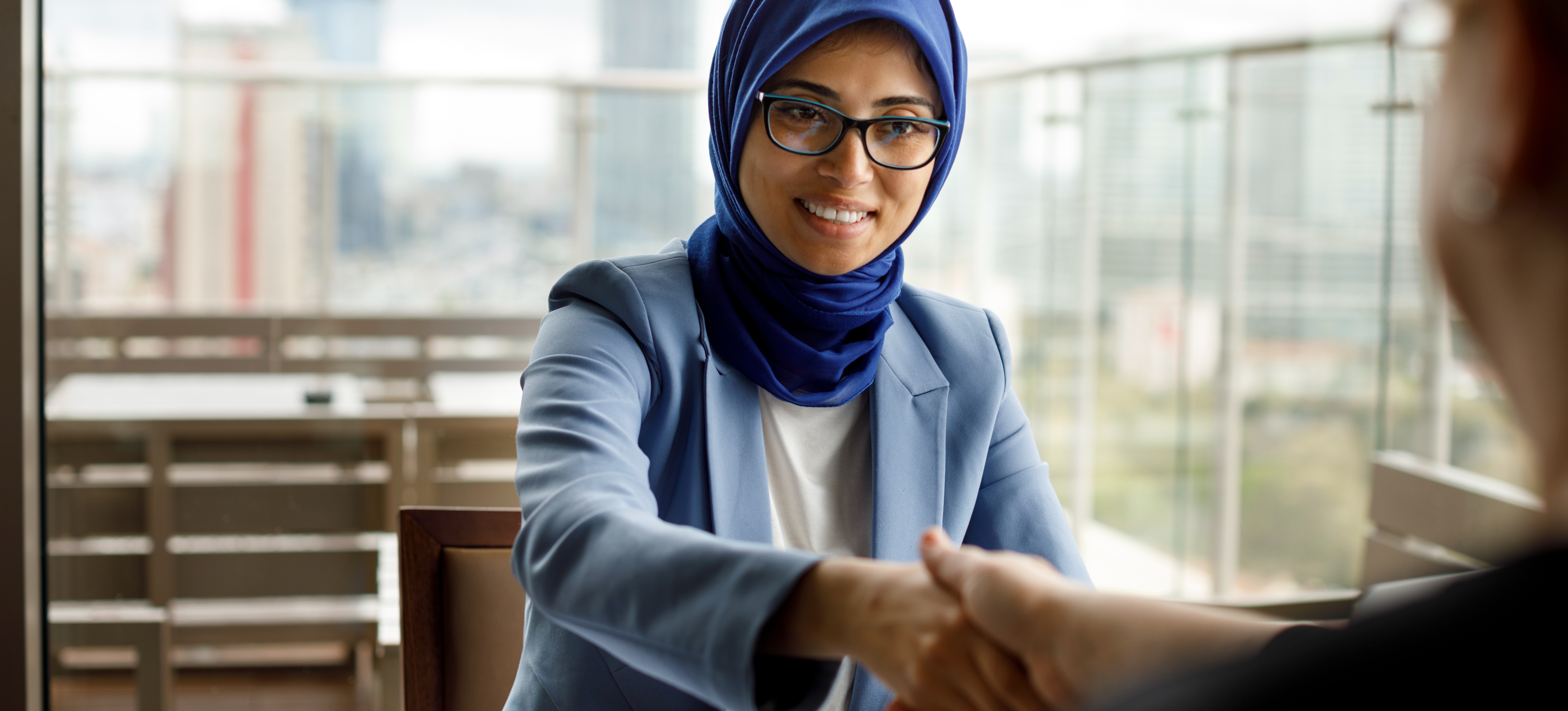 [Featured Image] A worker in a hijab shakes hands across a restaurant table. 