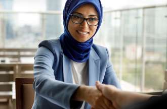 [Featured Image] A woman in a hijab shakes hands across a restaurant table. 