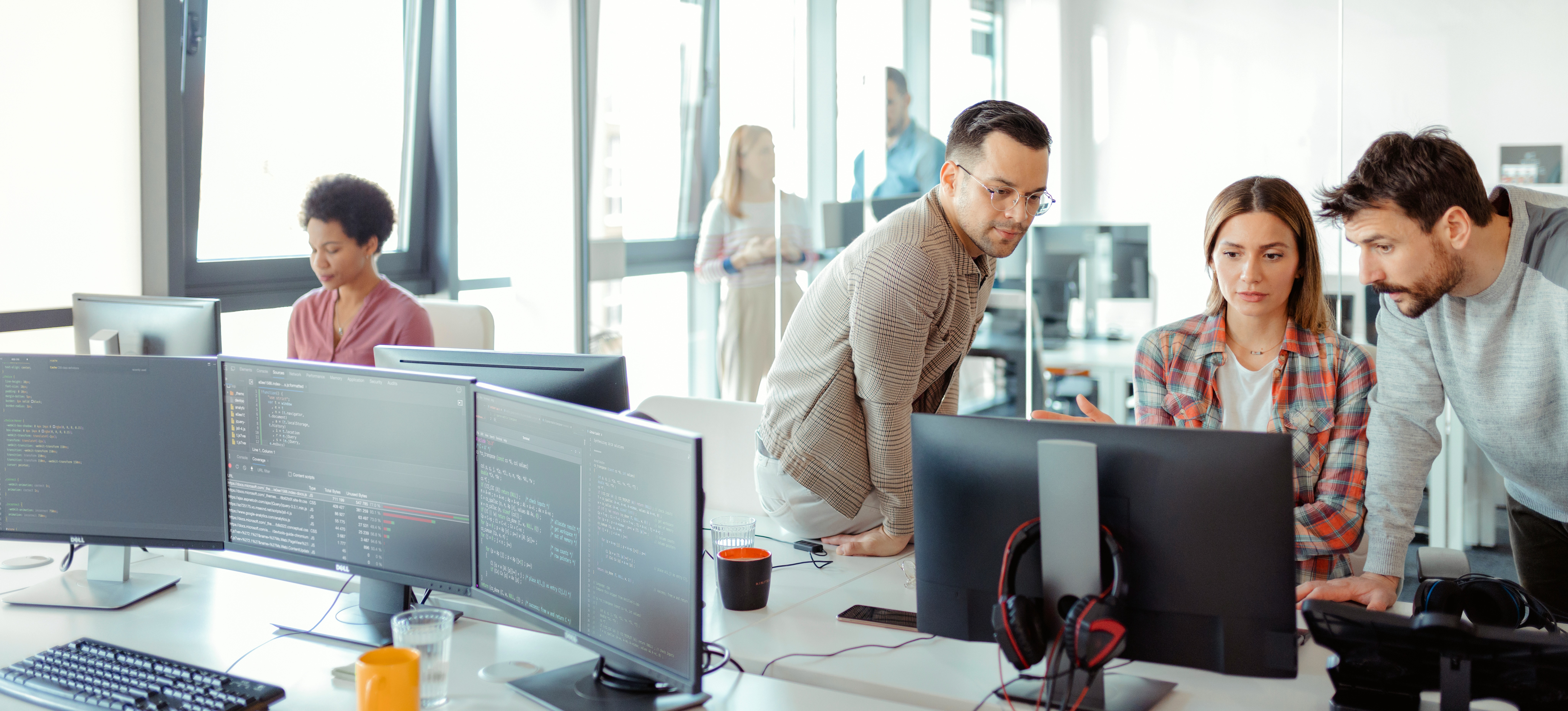 [Featured Image] Three members of a DevOps team look at a computer screen and discuss software development operations.
