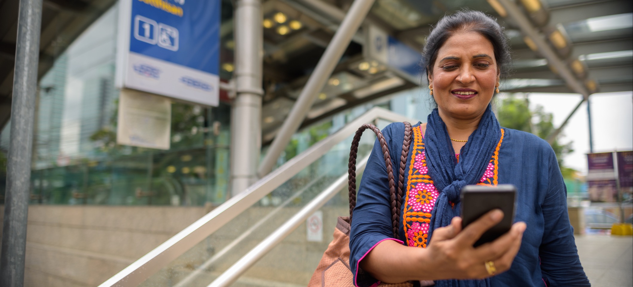 [Featured Image] A woman looks at a phone outside an office building. 