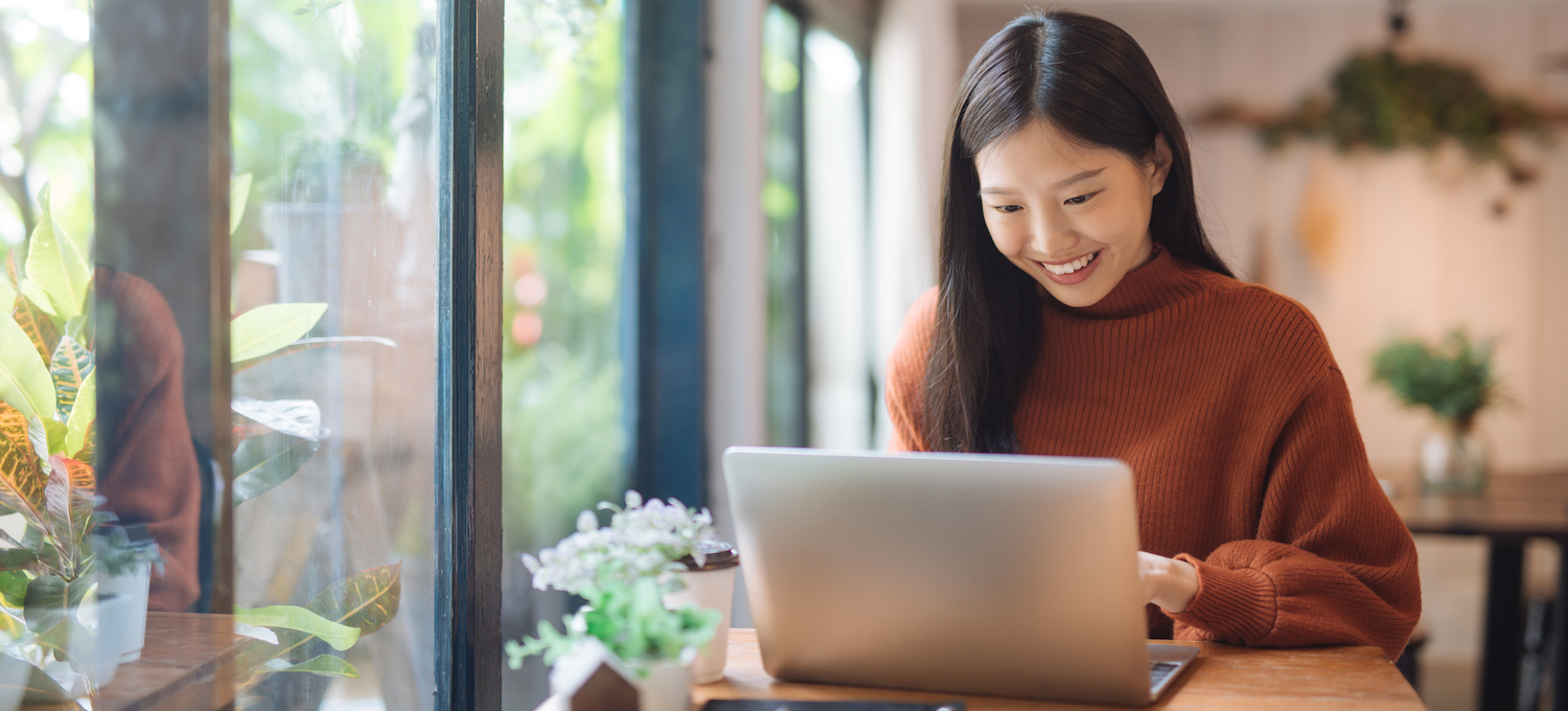 [Featured image] A person in a burnt orange sweater sits in a room filled with plants, working on their laptop. 