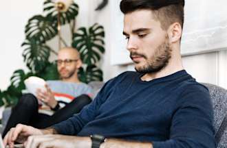 [Featured image] Two men sit in a living room, one working on data analysis on his laptop