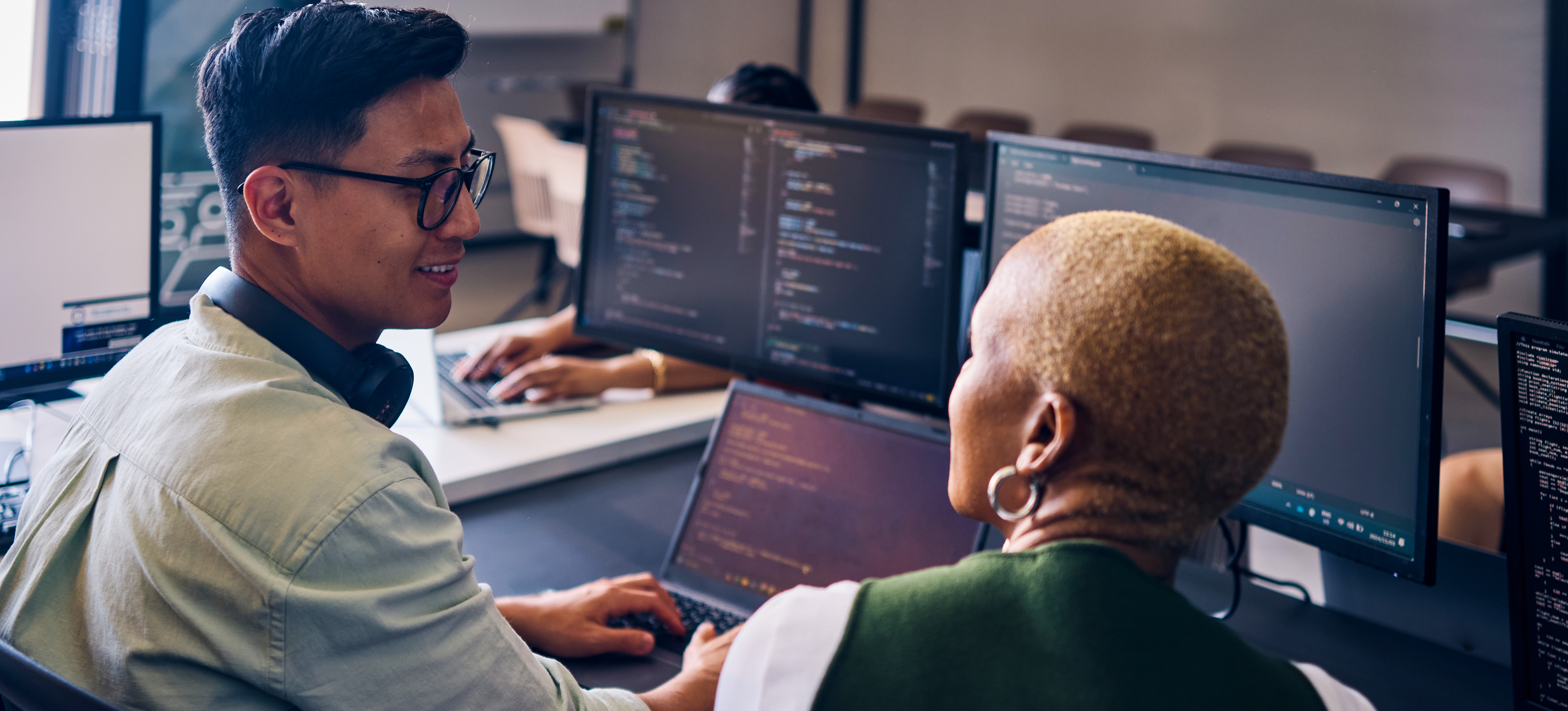 [Featured Image] Software engineers analyze code in a work environment while discussing how long it takes to learn software engineering.