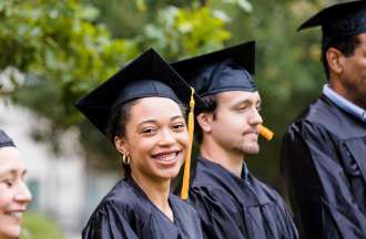 [Featured Image]: Two Men and two women in black cap and gowns wait to get their early childhood education degrees.