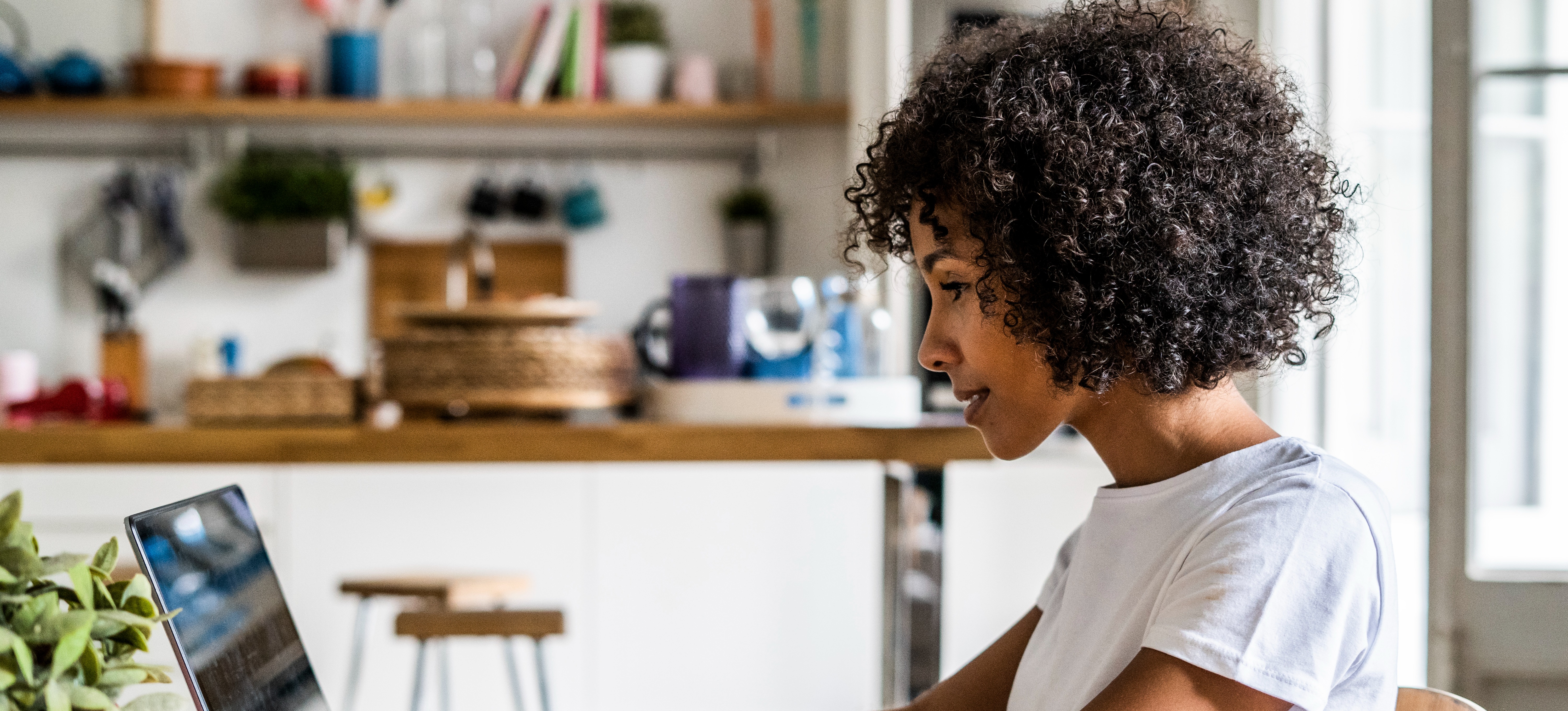 [Featured Image] An employee does remote work on their laptop from their kitchen at home. 
