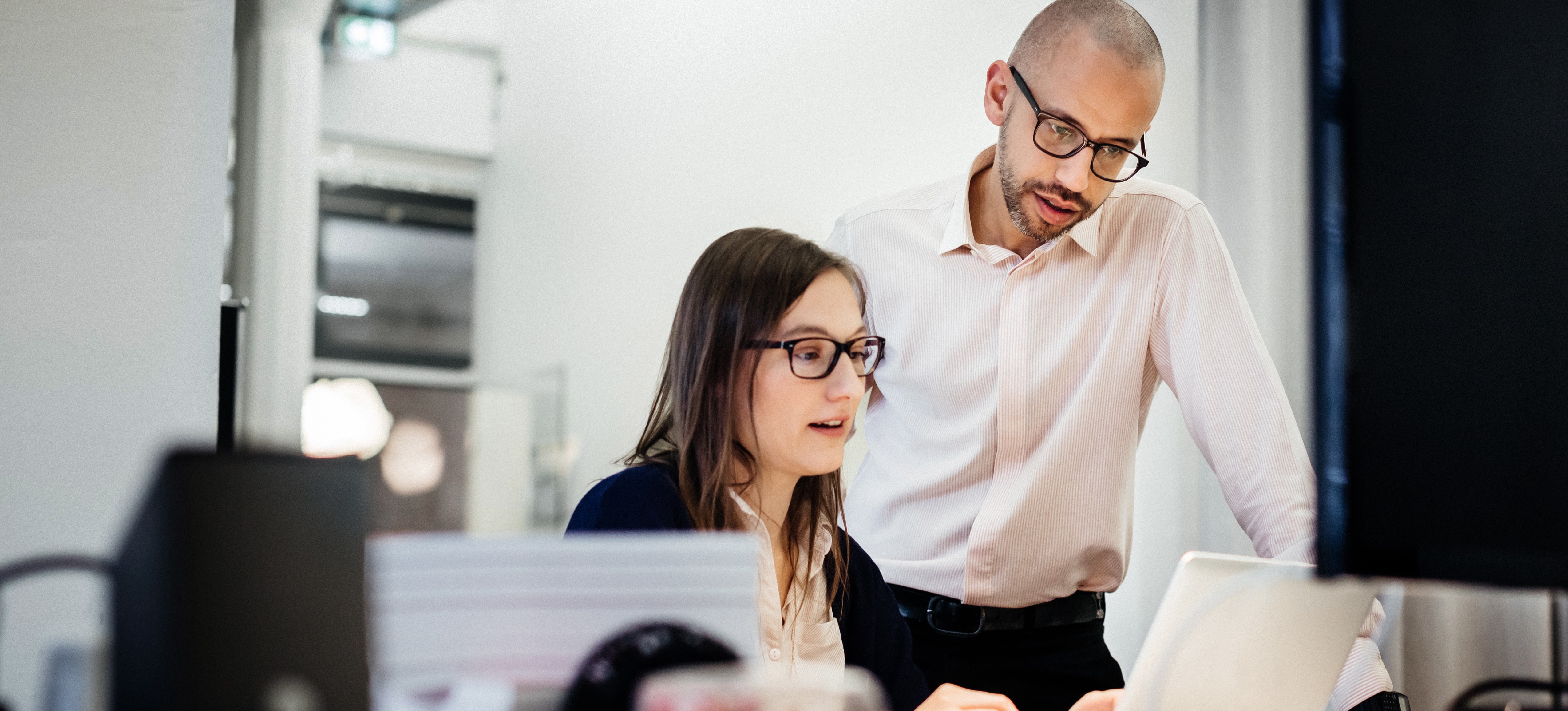 [Featured Image] Two work colleagues discuss pen tester certification as they look at a computer screen.
