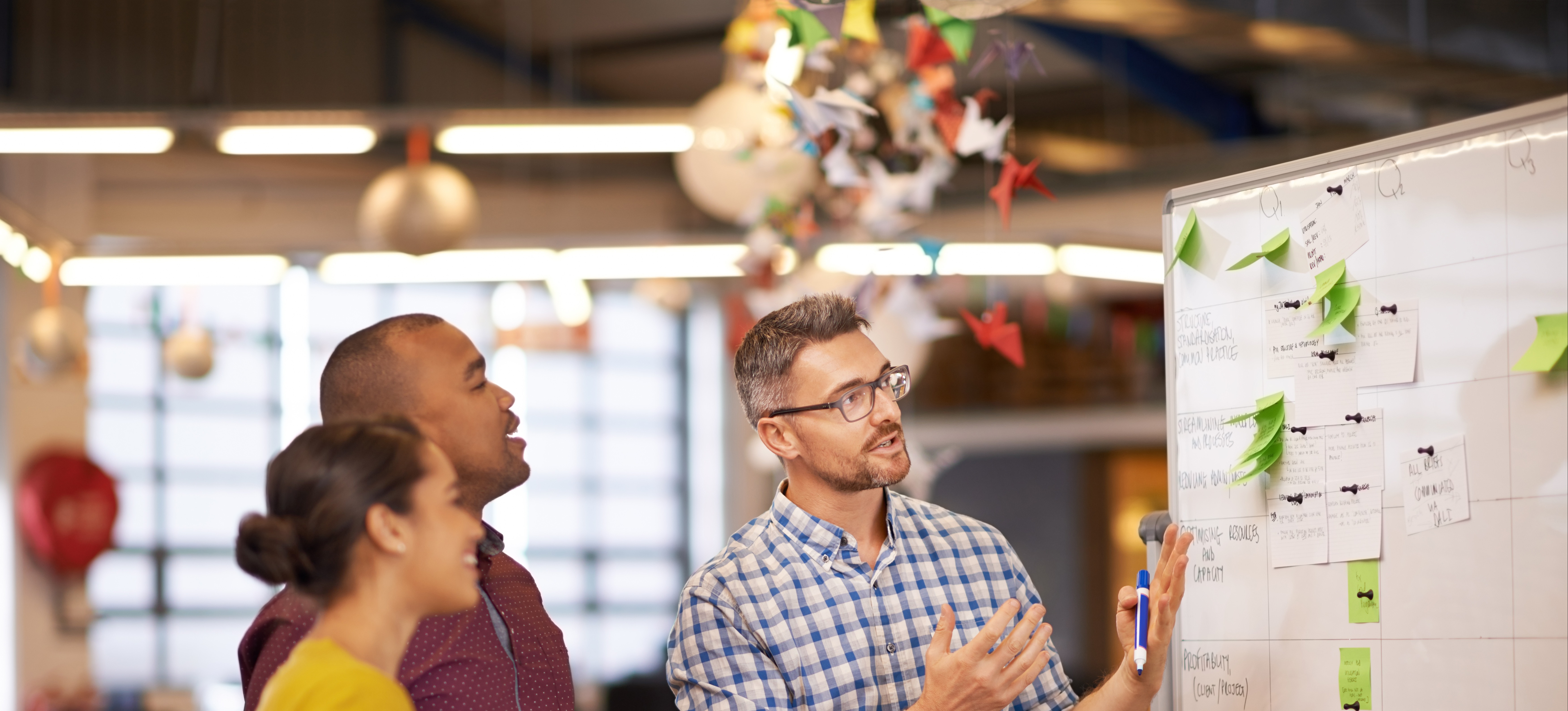 [Featured Image]: Agile Project Manager, wearing a plaid shirt, is analyzing information with members of the team. 