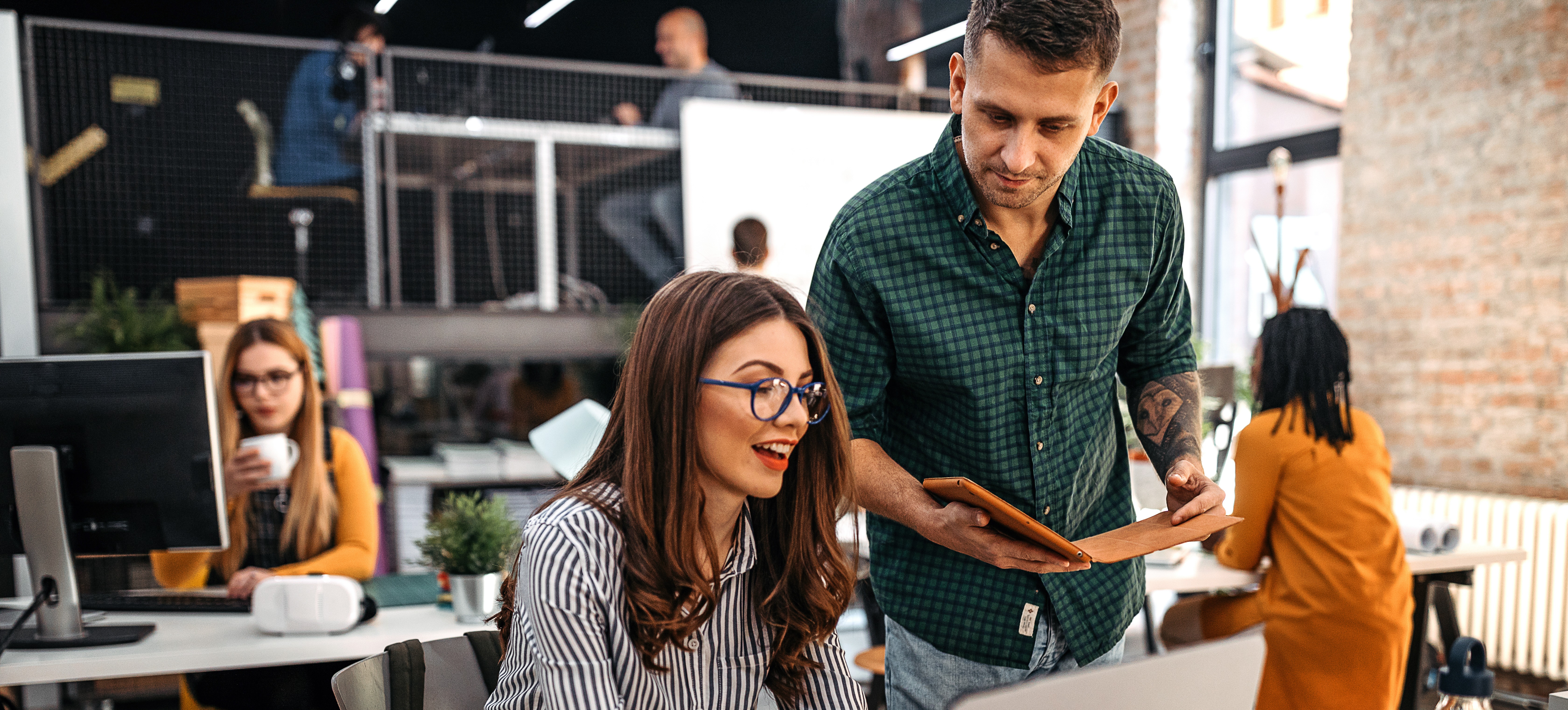 [Featured Image]:   A male, wearing a green shirt and a female wearing a black and white patterned top, sitting in front of her laptop, are meeting to discuss the latest strategy. 