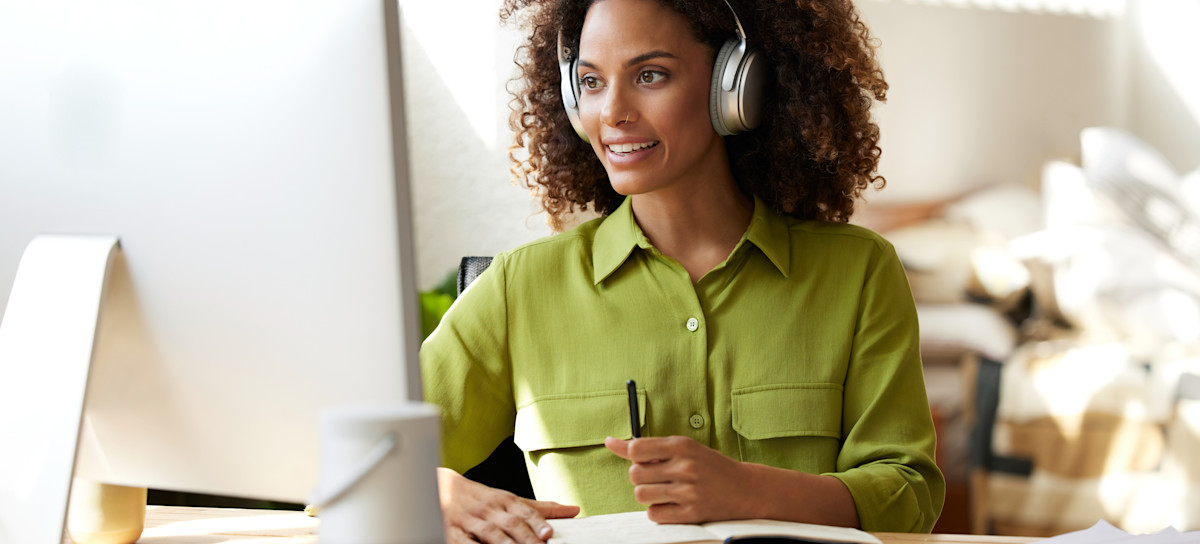 [Featured Image] A smiling worker wearing headphones sits at their home office desk with a computer, journal, and papers, working at a job they have gotten after majoring in English.
