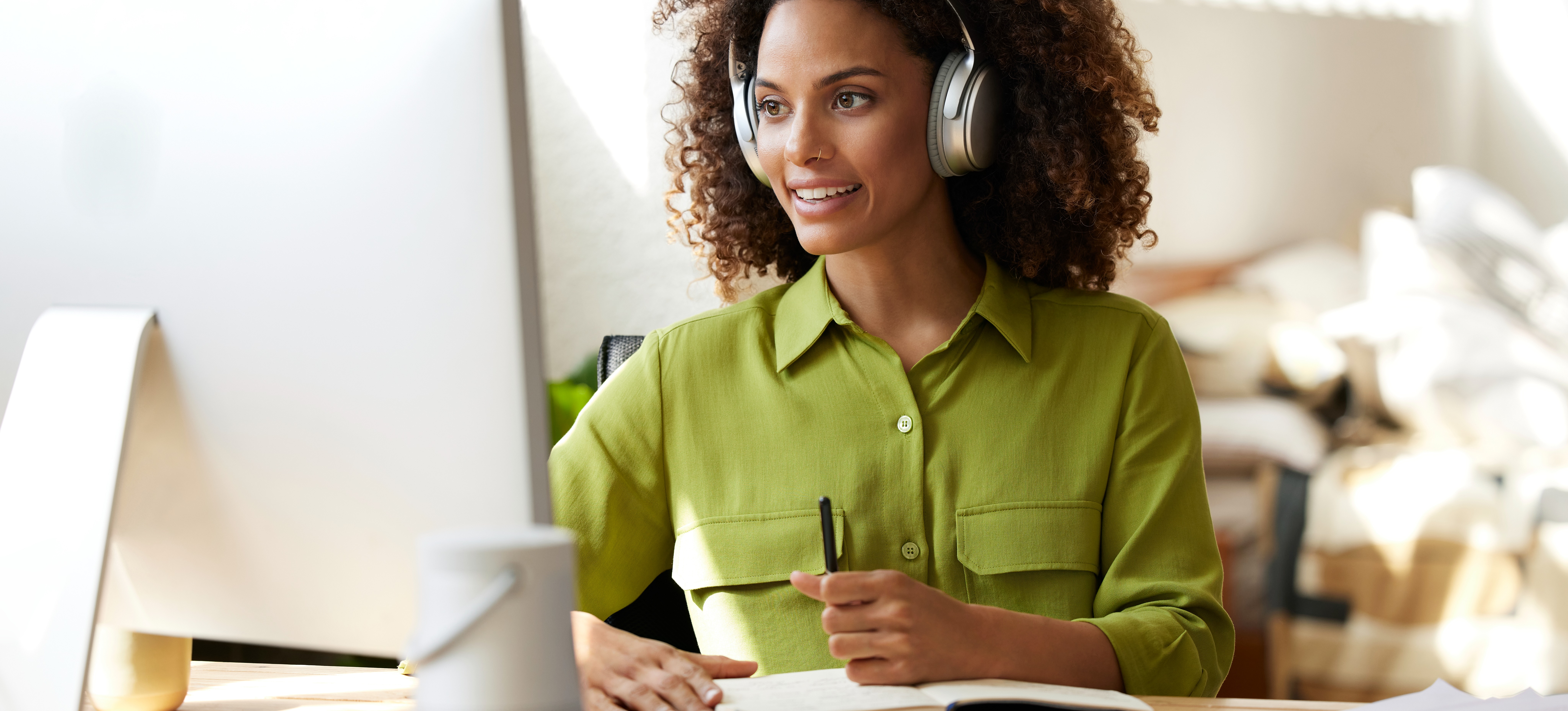[Featured Image] A smiling worker wearing headphones sits at their home office desk with a computer, journal, and papers, working at a job they have gotten after majoring in English.
