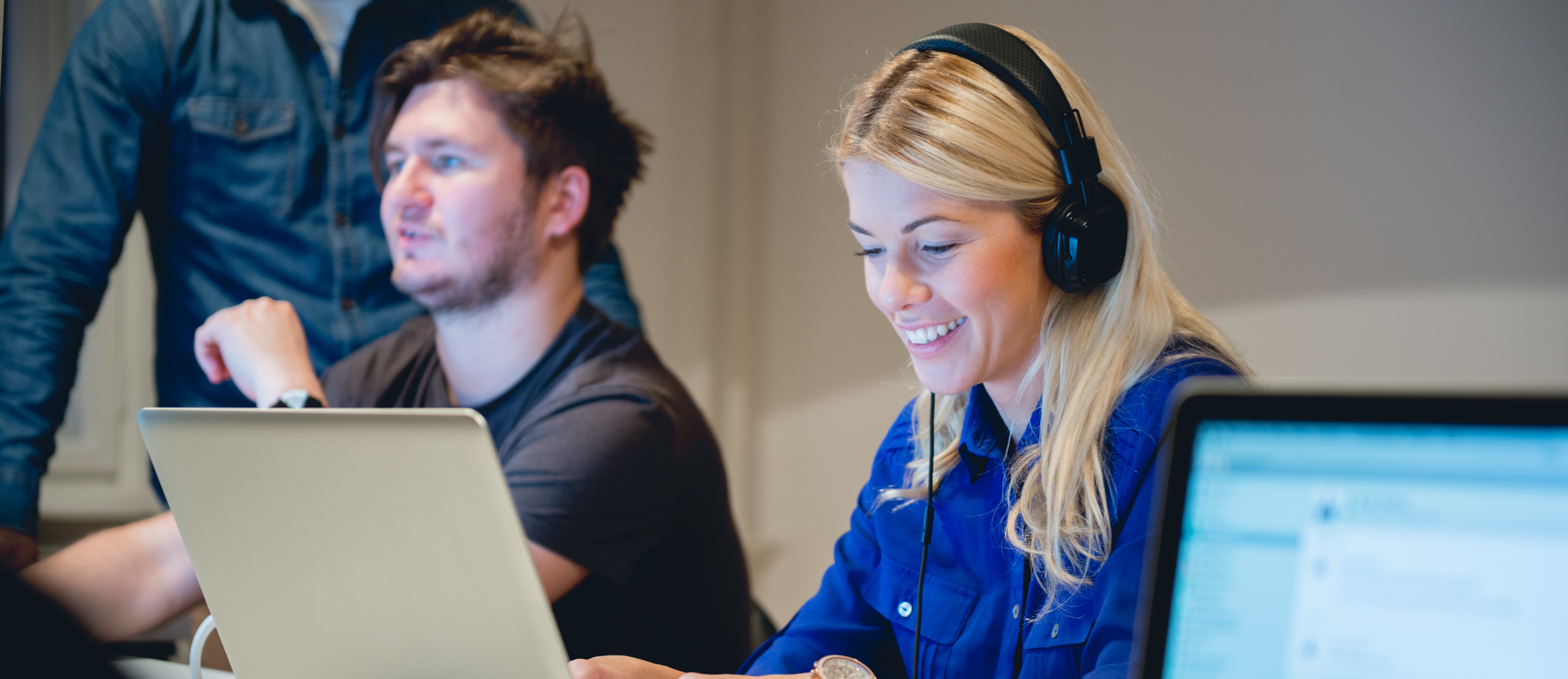 [Featured image] A person wearing headphones works on a laptop in a computer science class.