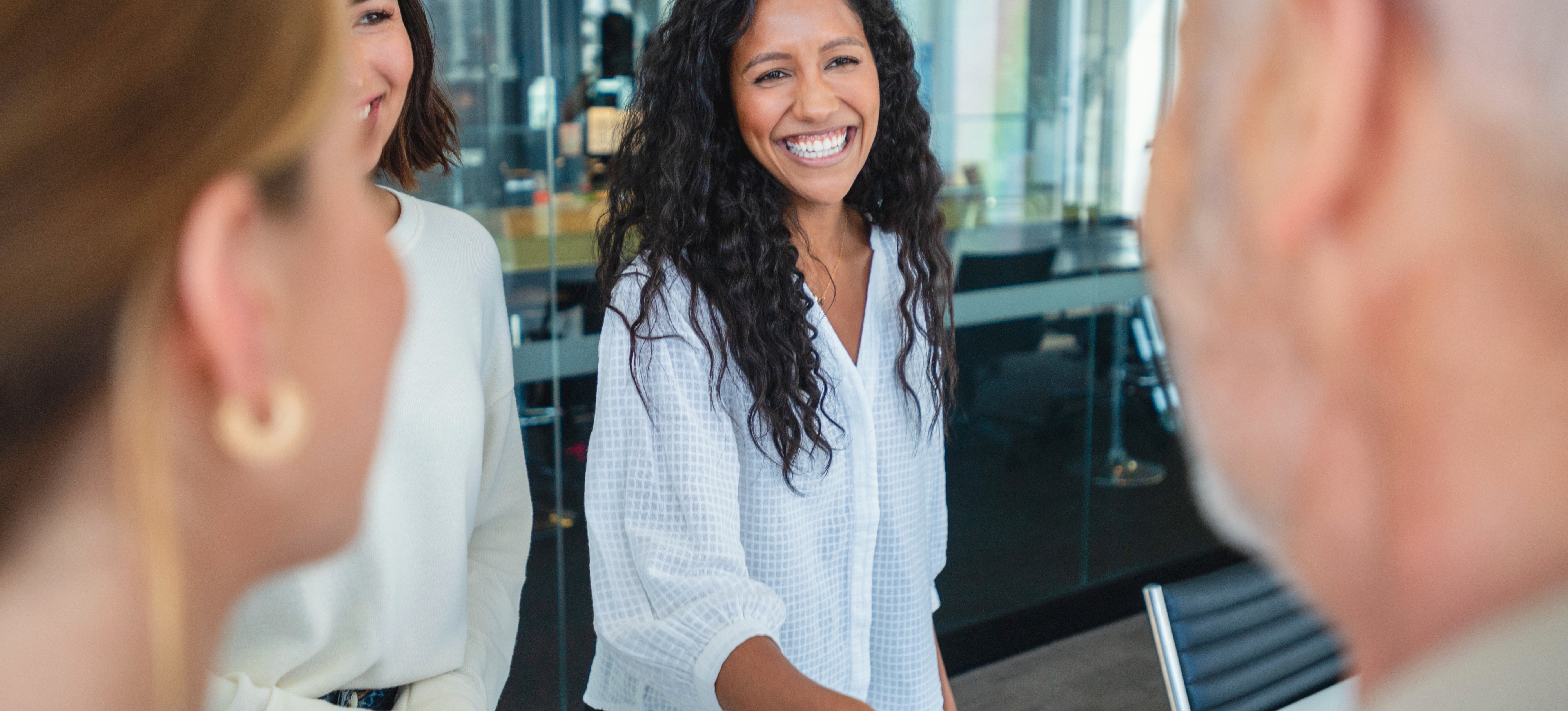 [Featured Image] A new employee smiles broadly as they shake the hand of her interviewer after receiving a job offer with a sign-on bonus as two other members of the interview team look on.